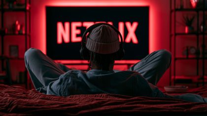 Mann sitzt mit Kopfhörern auf dem Sofa vor dem Fernseher, auf dem ein Netflix-Logo ist.