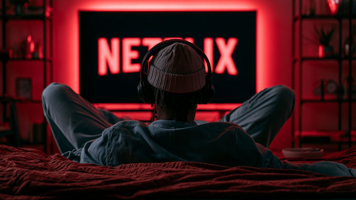 Mann sitzt mit Kopfhörern auf dem Sofa vor dem Fernseher, auf dem ein Netflix-Logo ist.
