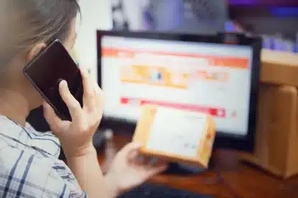 Hände halten ein Smartphone mit Vorbestellungsbestätigung, Einkaufstasche daneben