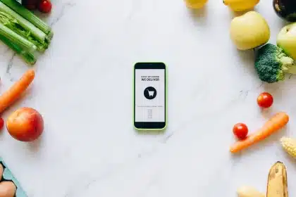 Hände halten Smartphone mit Rabattcode über Laptop beim Online-Einkauf