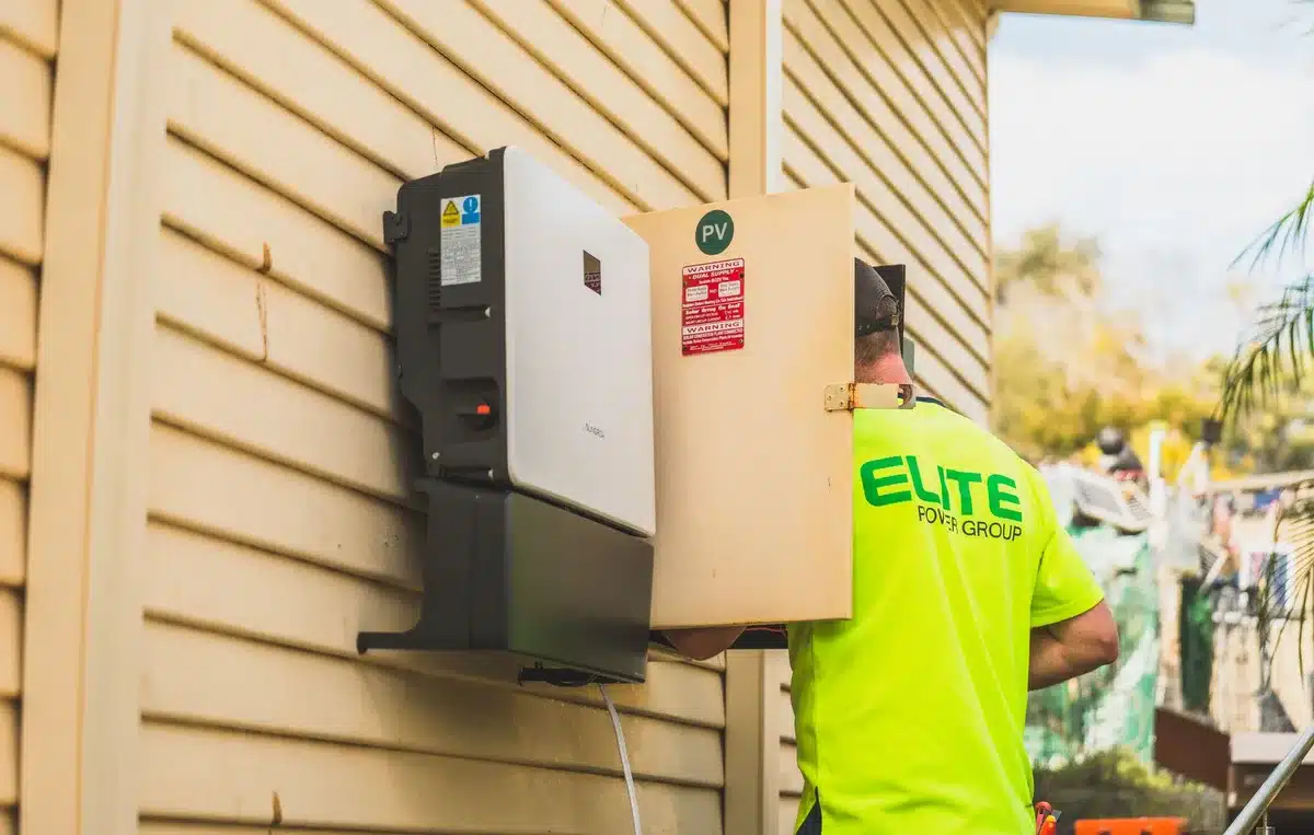 Ein Wechselrichter montiert an einer Hauswand neben Solarmodulen