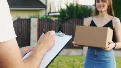 Hand auf einer Paketwaage in einem Zolllager mit gestapelten Paketen im Hintergrund