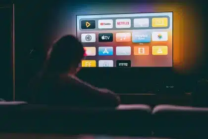 Fernbedienung auf einem Couchtisch vor einem leuchtenden Fernseher in einem Wohnzimmer