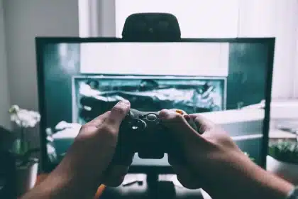 Hände an einem Controller vor TV im Wohnzimmer, stimmungsvolles Licht