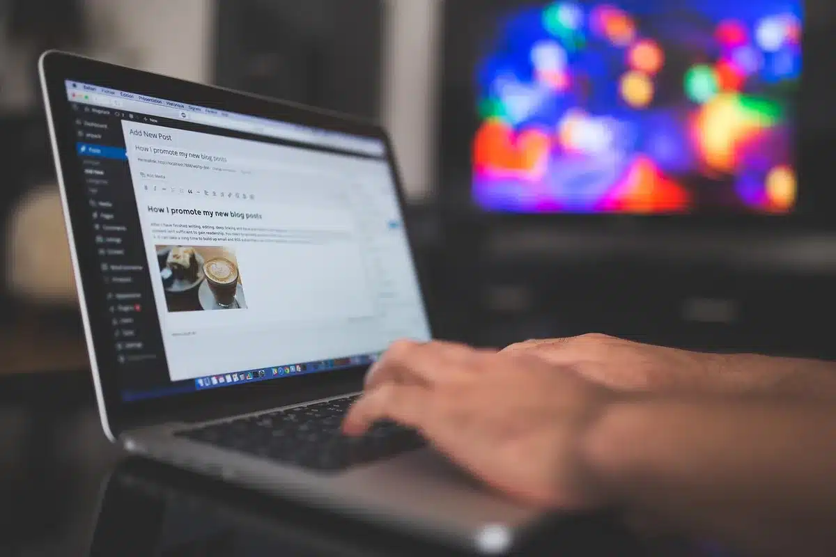 Laptop mit Hand am Trackpad, Notizblock und Kopfhörer auf einem hellen Schreibtisch