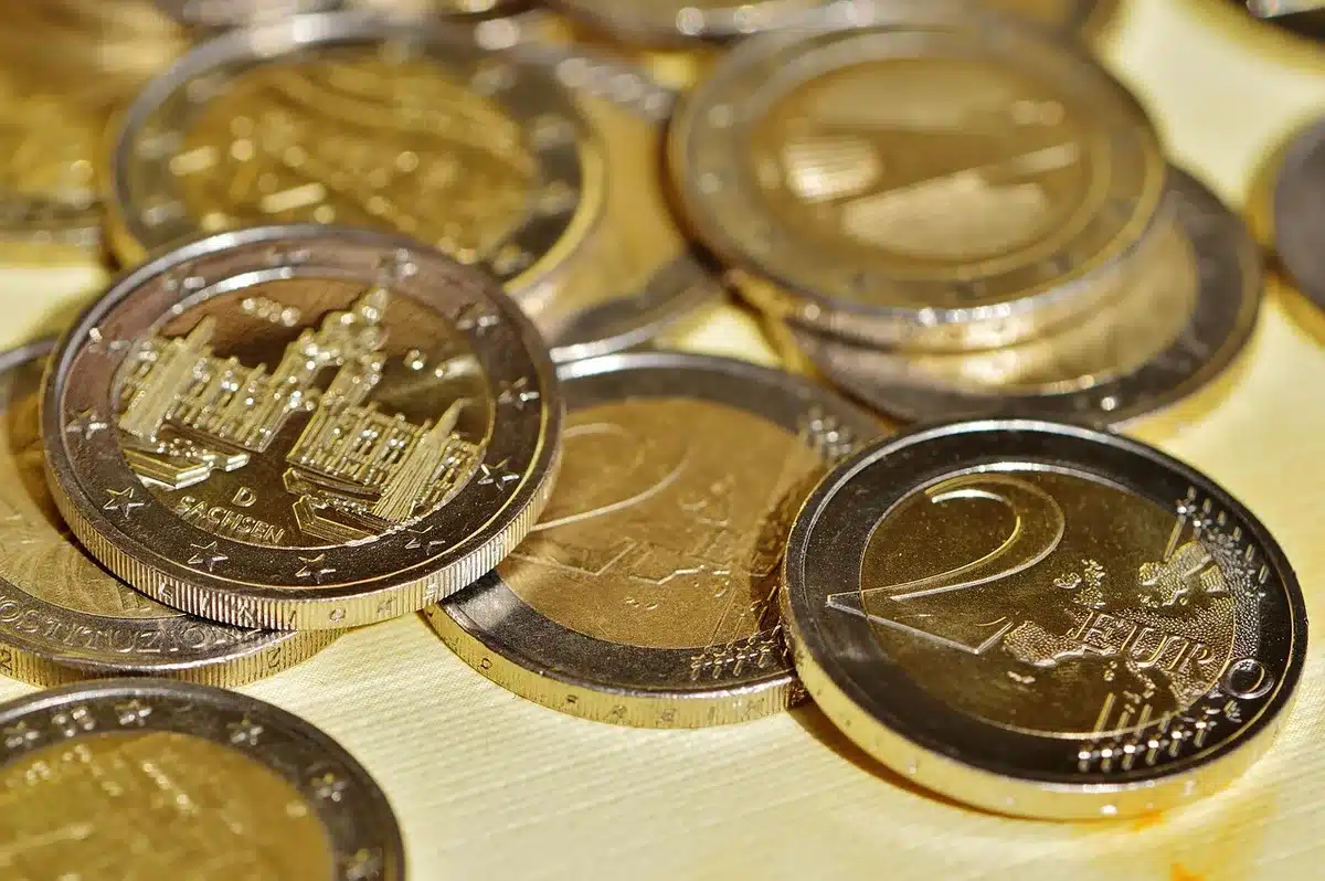 Hände zählen Euro-Münzen neben Laptop und kleinem Sparbuch auf Holztisch